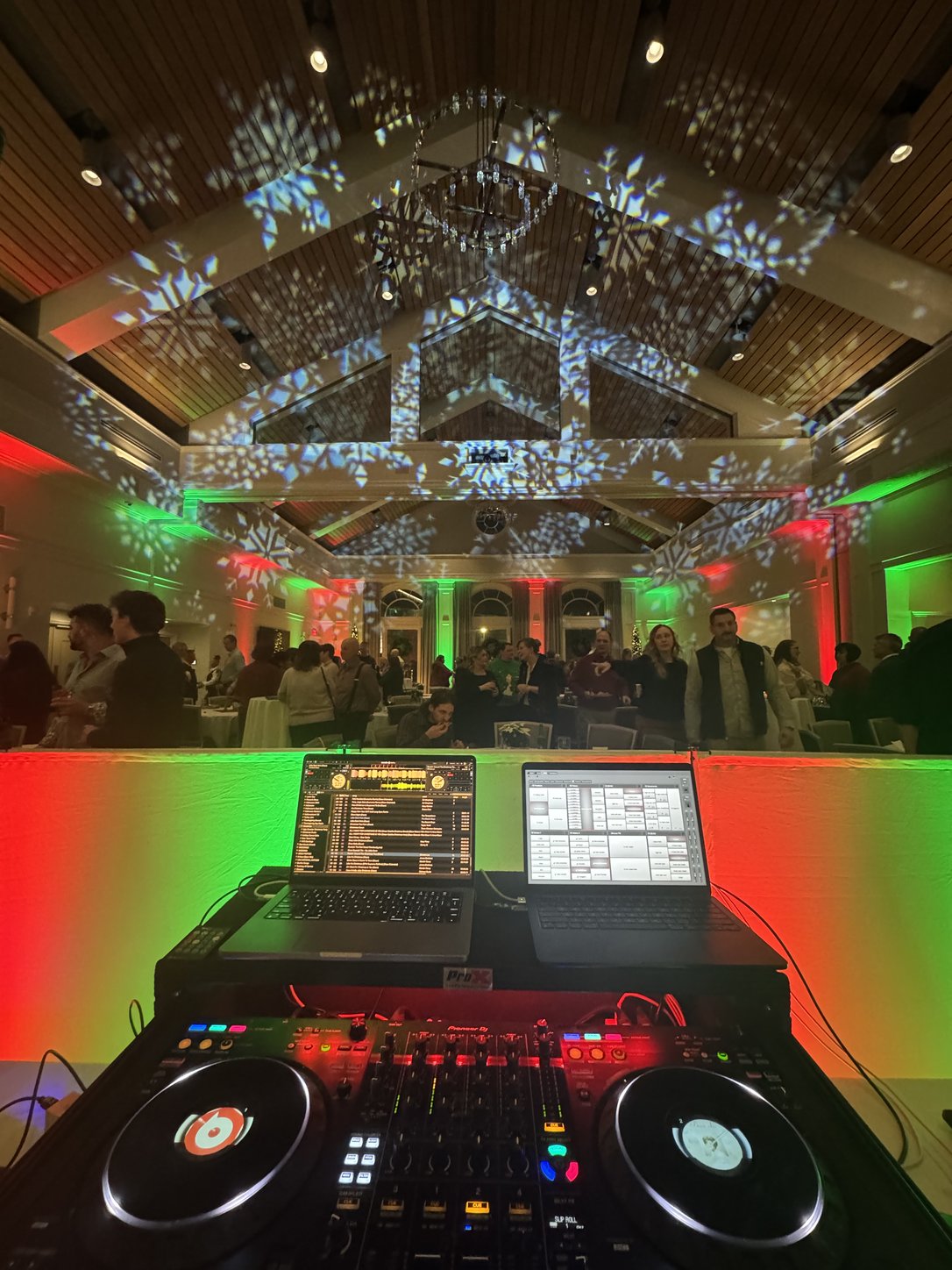A company holiday party seen from the DJ booth — snowflake gobos across a vaulted ceiling with the room washed in red and green