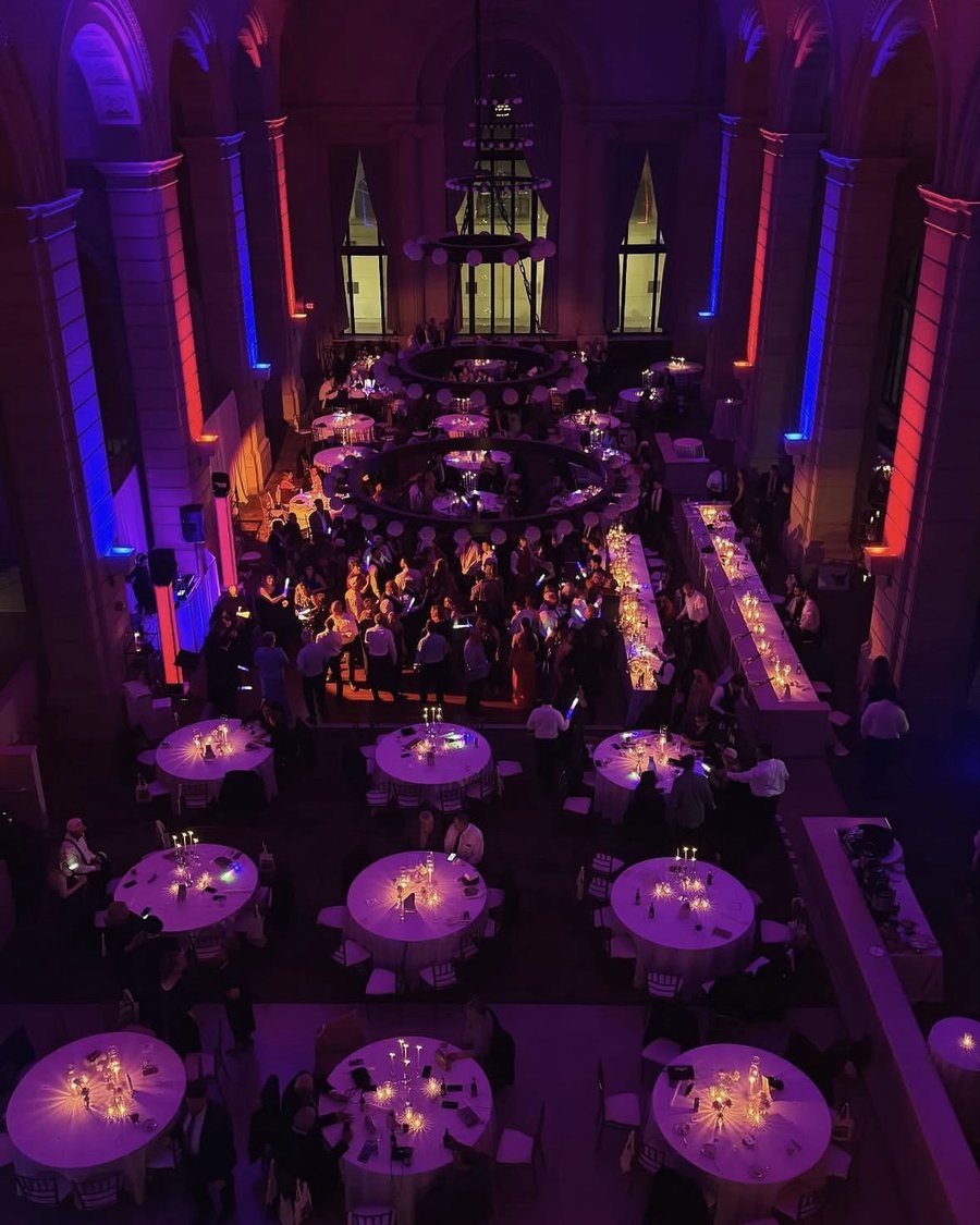 A reception in a grand hall, columns washed in red and blue up-lighting above a packed dance floor